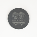 A round dark gray slate coaster with a light gray engraved design featuring flames and the text 'BANNED BOOK READER', shown on a plain white background.