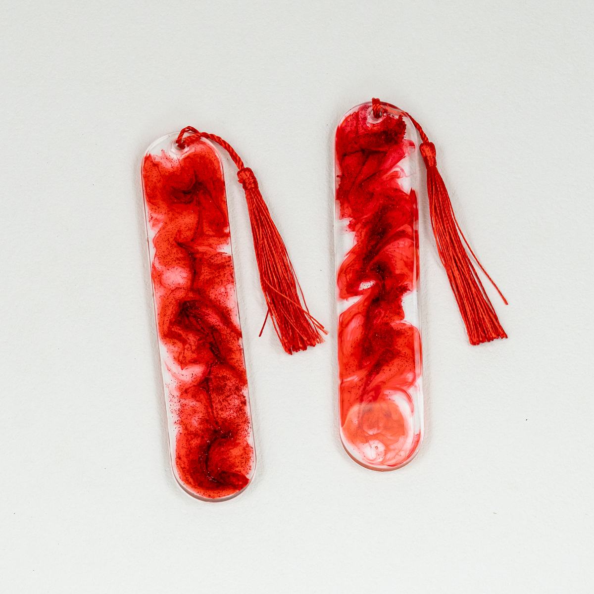 Two oval clear and red resin bookmarks with blood-like swirls and glitter, including red tassels.