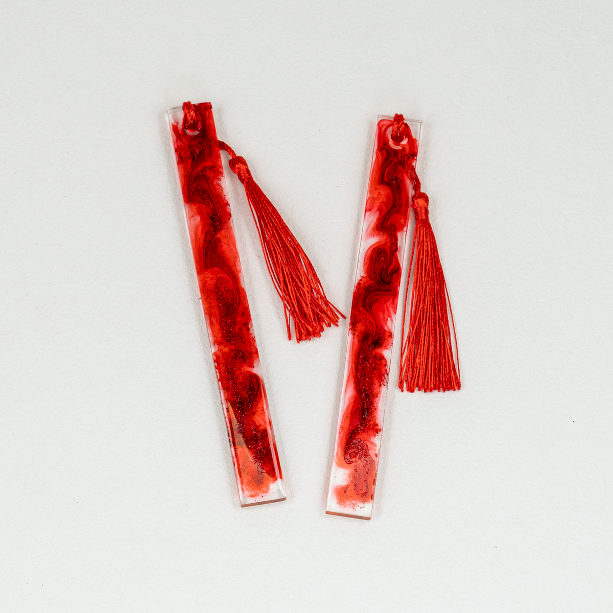 Two slim rectangle clear and red resin bookmarks with blood-like swirls and glitter, including red tassels.