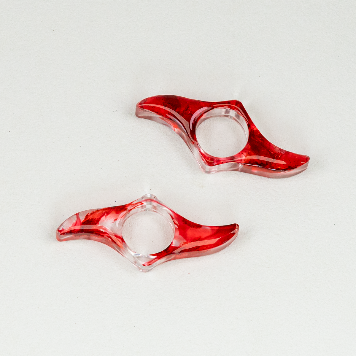 Two clear and red blade shaped book page holders with blood-like swirls and glitter on white background.