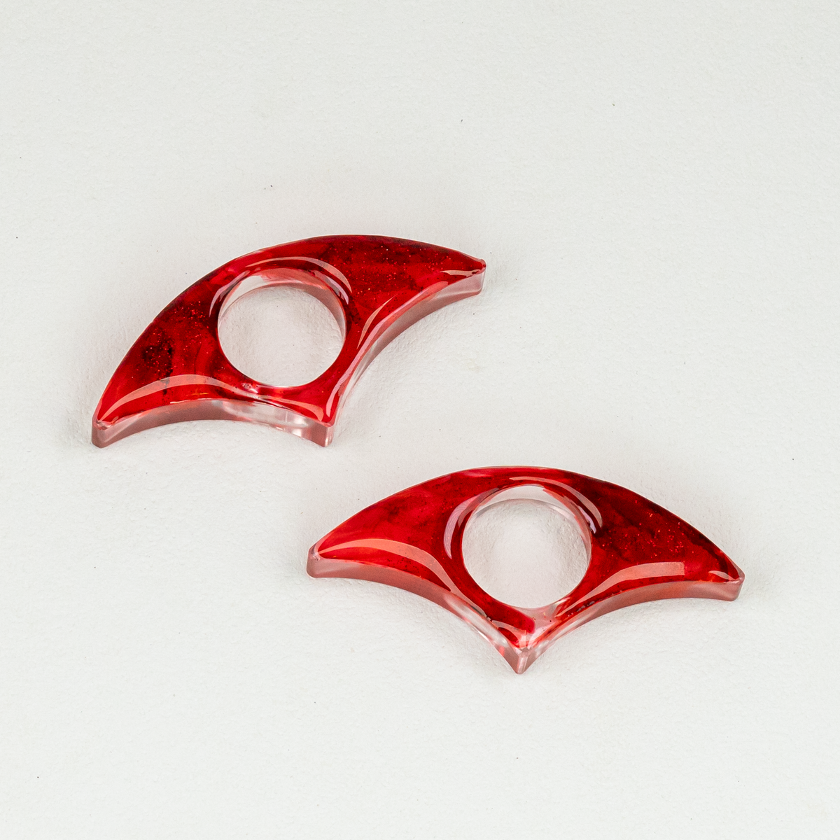 Two clear and red resin fan shaped book spreaders with blood-like glitter on a white background.