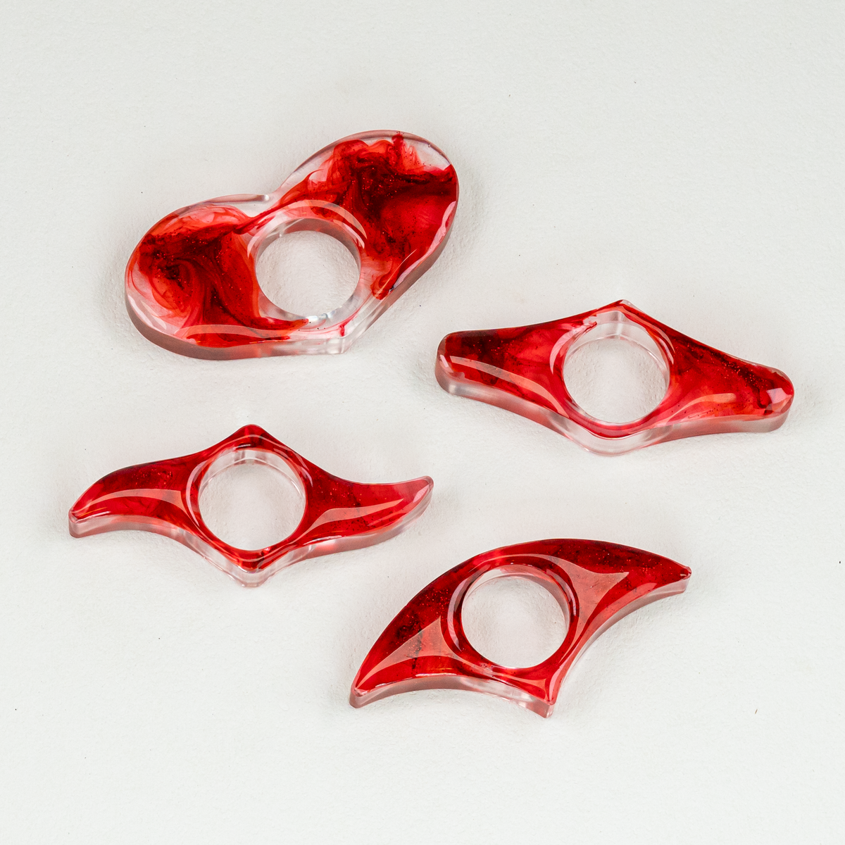 Four clear resin and red blood-like swirl page spreaders with glitter in the shape of a heart, blade, wing, and fan.