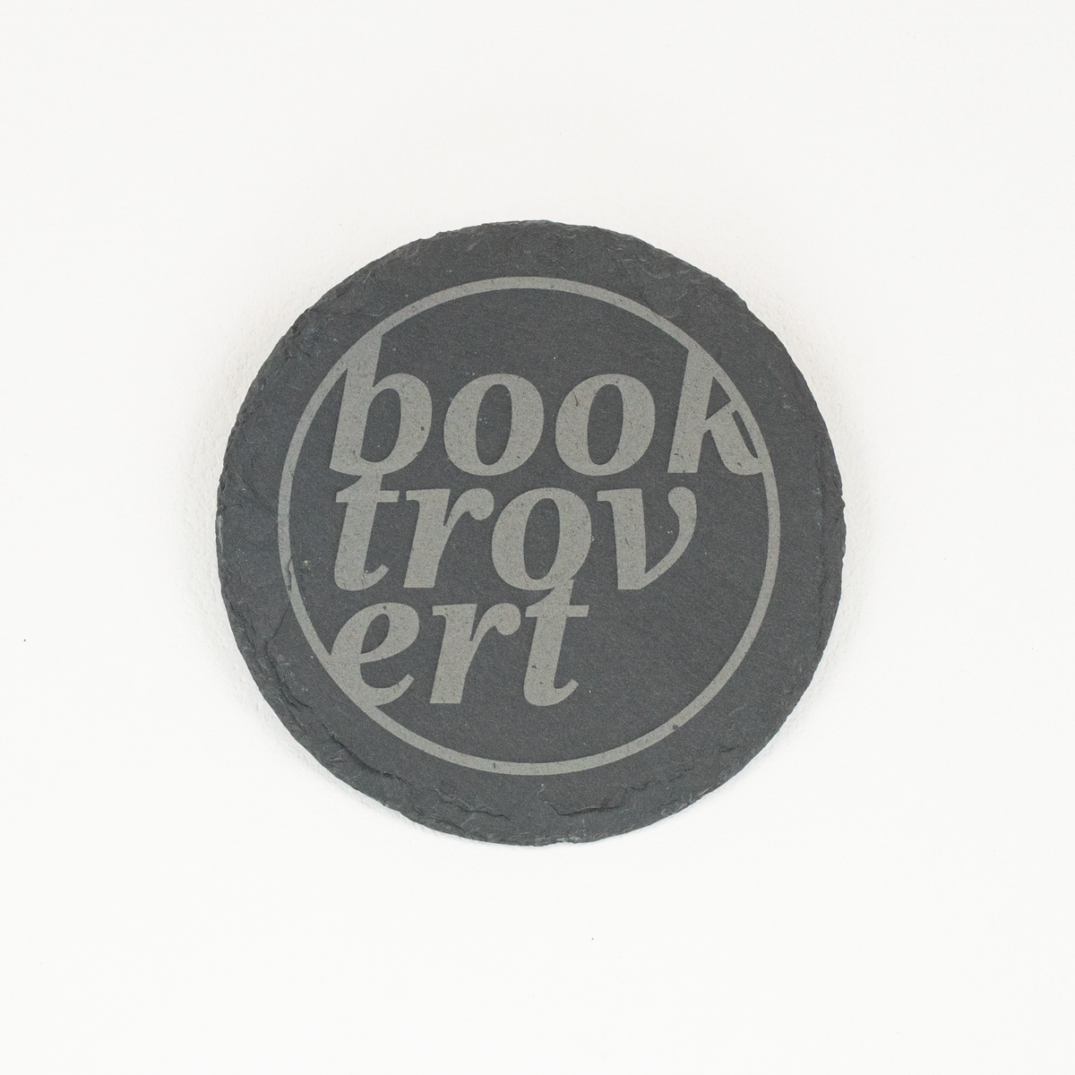 A round dark gray slate coaster with the words 'Booktrovert' printed in a light gray stylized font, centered on a plain white background.