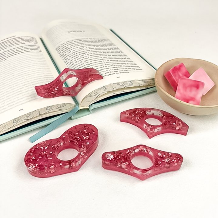 Four resin pink and foil page spreaders, styled on open book with bowl of wax melts.