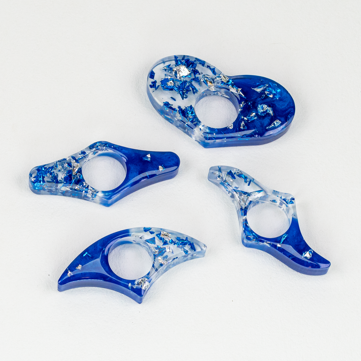 Four resin thumb page holders with half cobalt and half clear resin with blue and silver foil flakes, on white background.