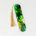 Oval shaped resin bookmark with gold and green swirls in clear resin with gold tassel.