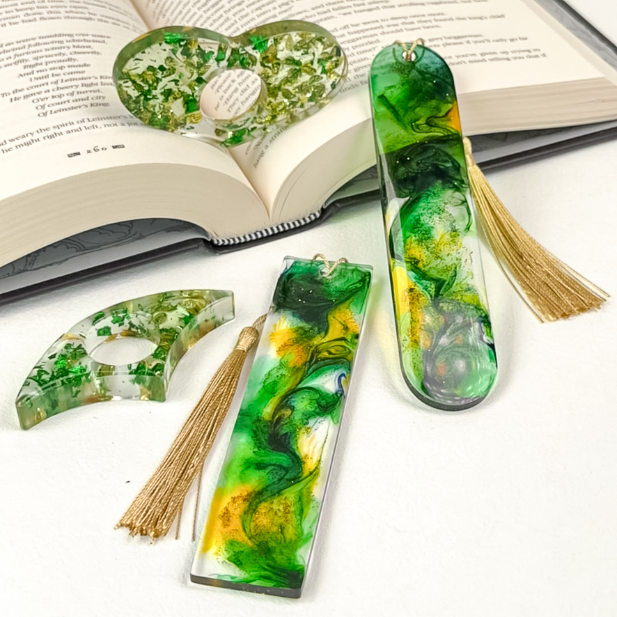 Two gold and emerald page spreaders styled on an open book, along side a rectangle and oval bookmark with green and gold flakes and gold tassels.