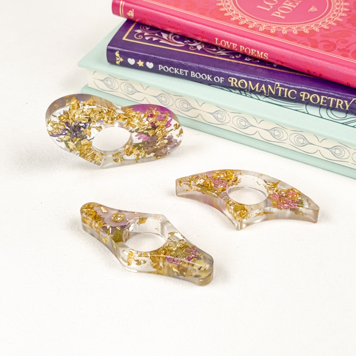 Three clear resin page holders with gold flakes and flowers, arranged by a stack of books.