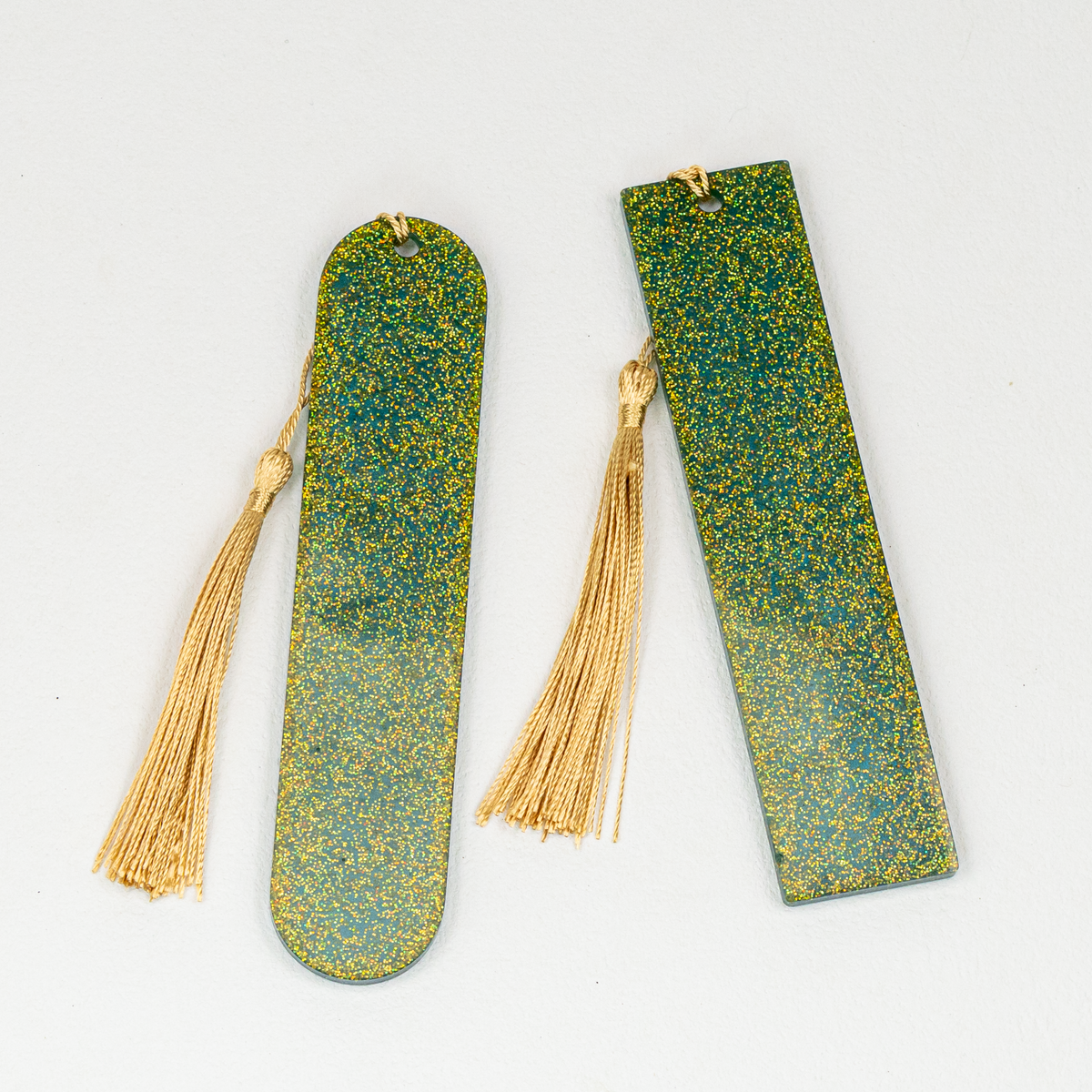 Reverse side of oval and rectangle resin bookmarks showing vibrant gold glitter and gold tassels