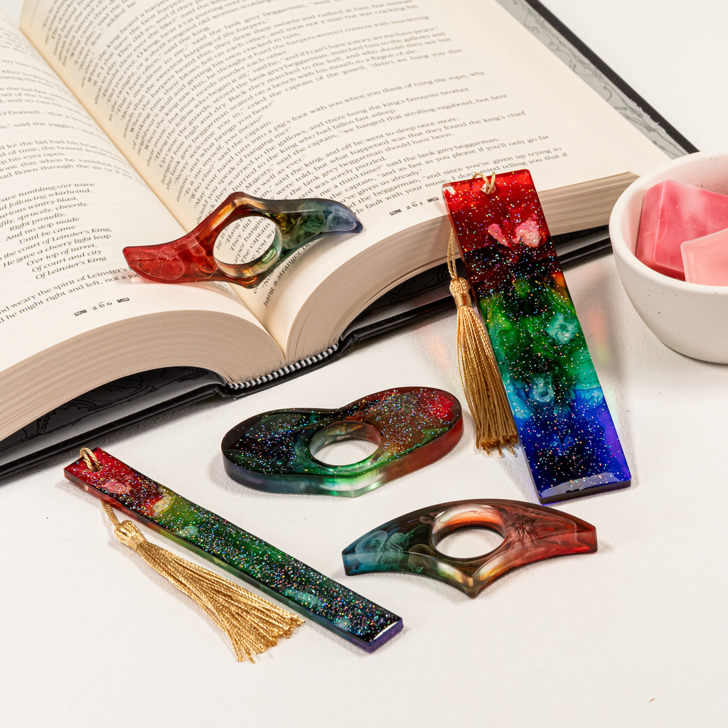 Collection of rainbow resin page holders and bookmarks arranged on open book with wax melts.