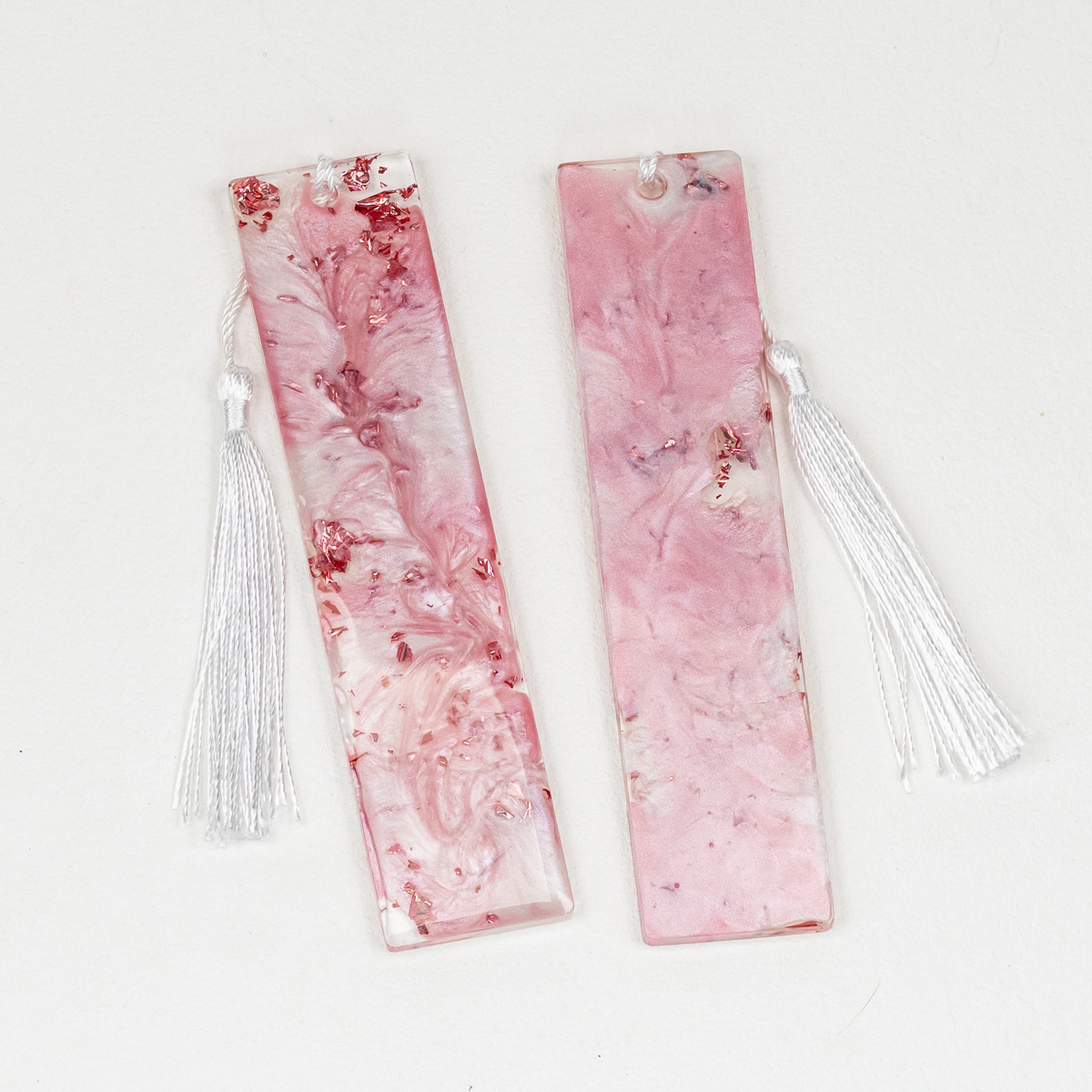 Two rectangle bookmarks, one reversed, with pink and white marbled resin and white tassels.