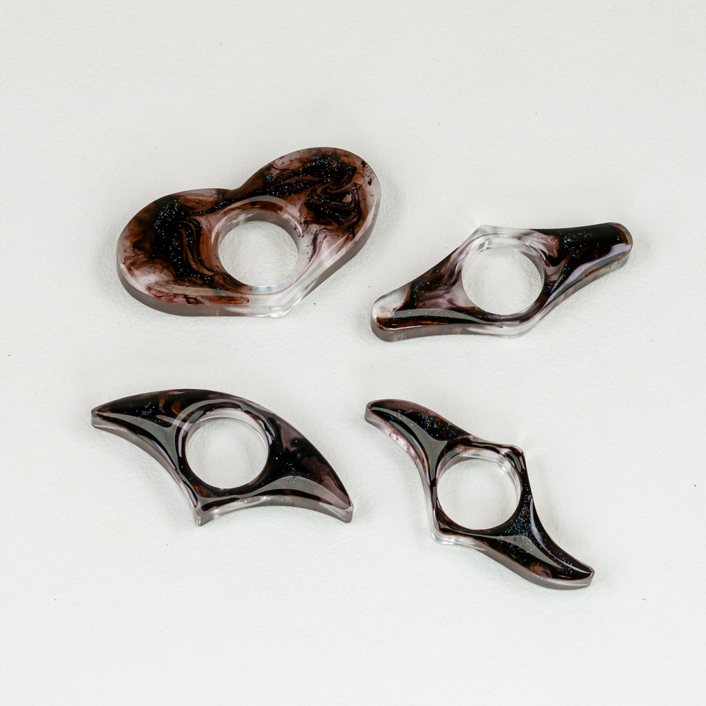 Four resin page holders with swirls of black wisps and glitter on white background.