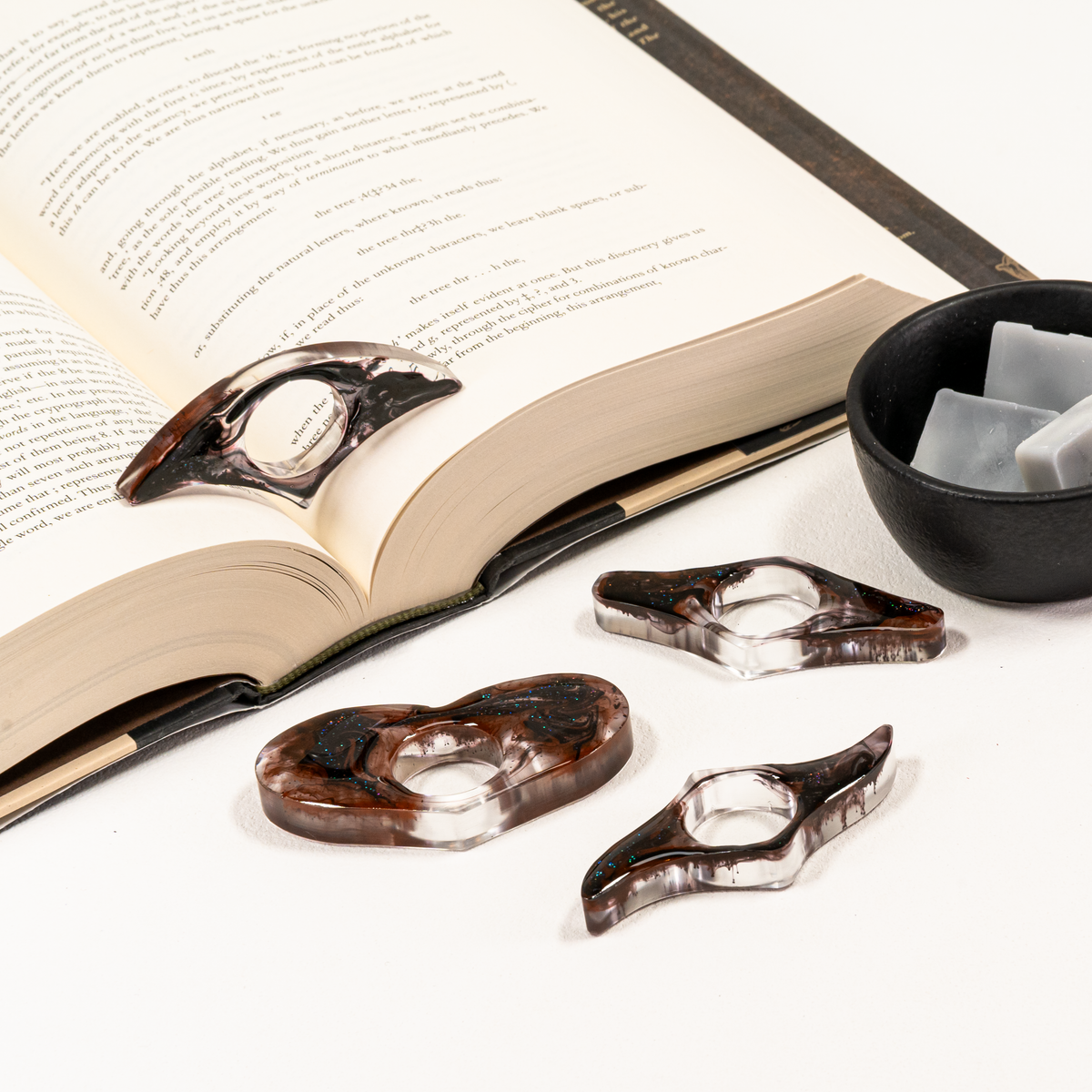 Four resin page holders with black wisp like variations, styled on open book and bowl of wax melts.