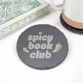 Round slate coaster with 'Spicy Book Club' and two chili peppers, styled next to a book and ceramic mug