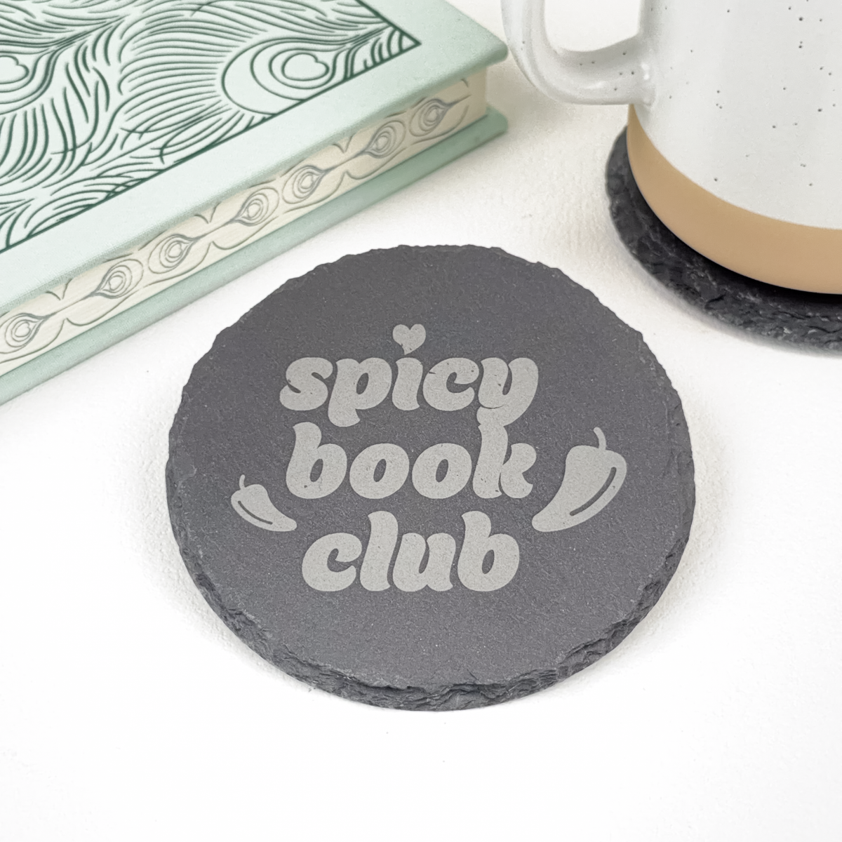 Round slate coaster with 'Spicy Book Club' and two chili peppers, styled next to a book and ceramic mug